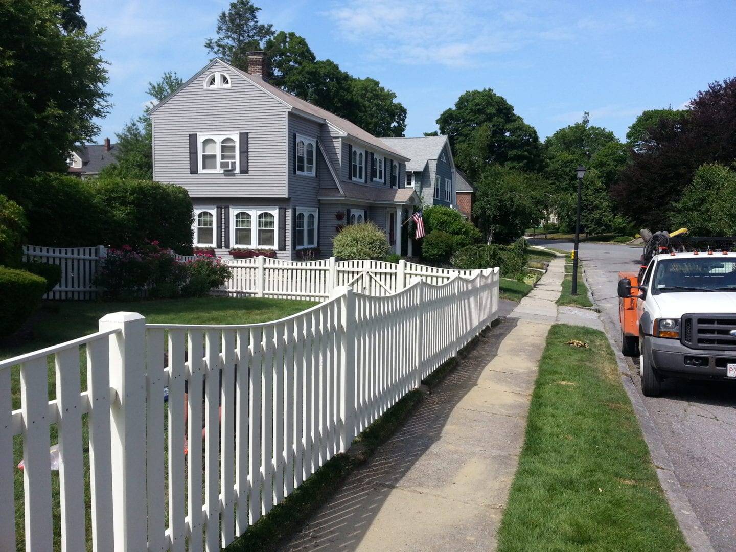 Well maintained appearance of the fence White picket fence curving along a sidewalk in front of a house