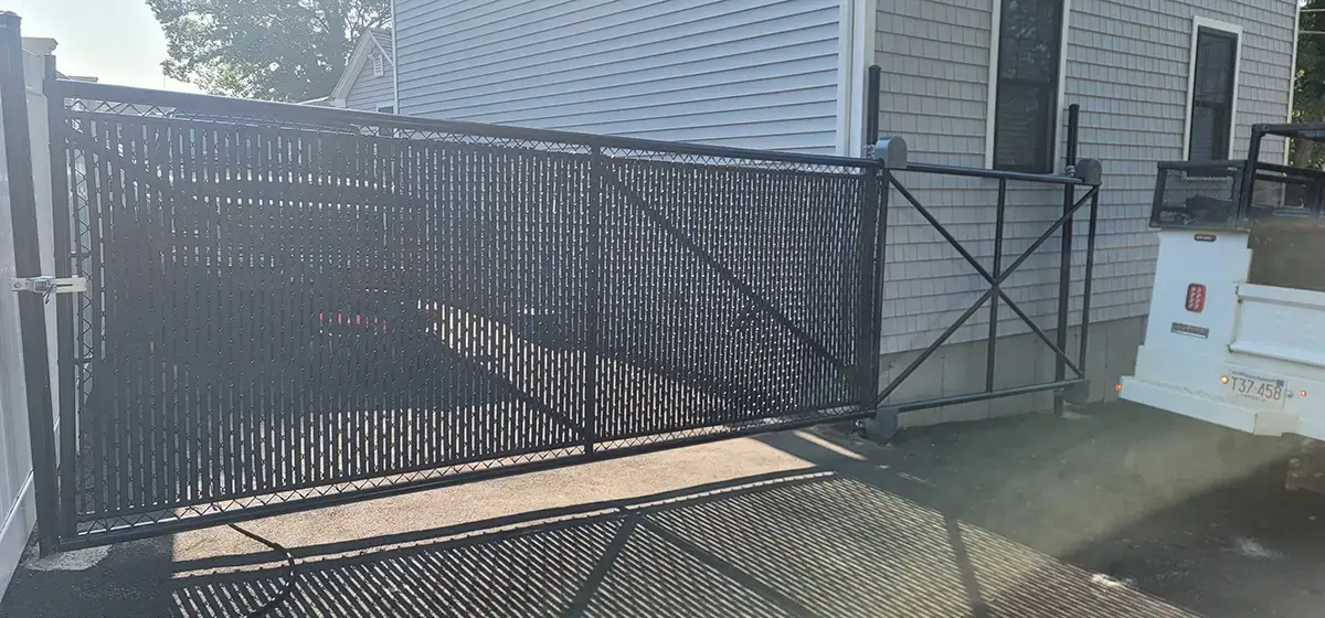 Custom Built Cantilever Slide Gate Black chain link roll gate with black privacy slats attached to a house