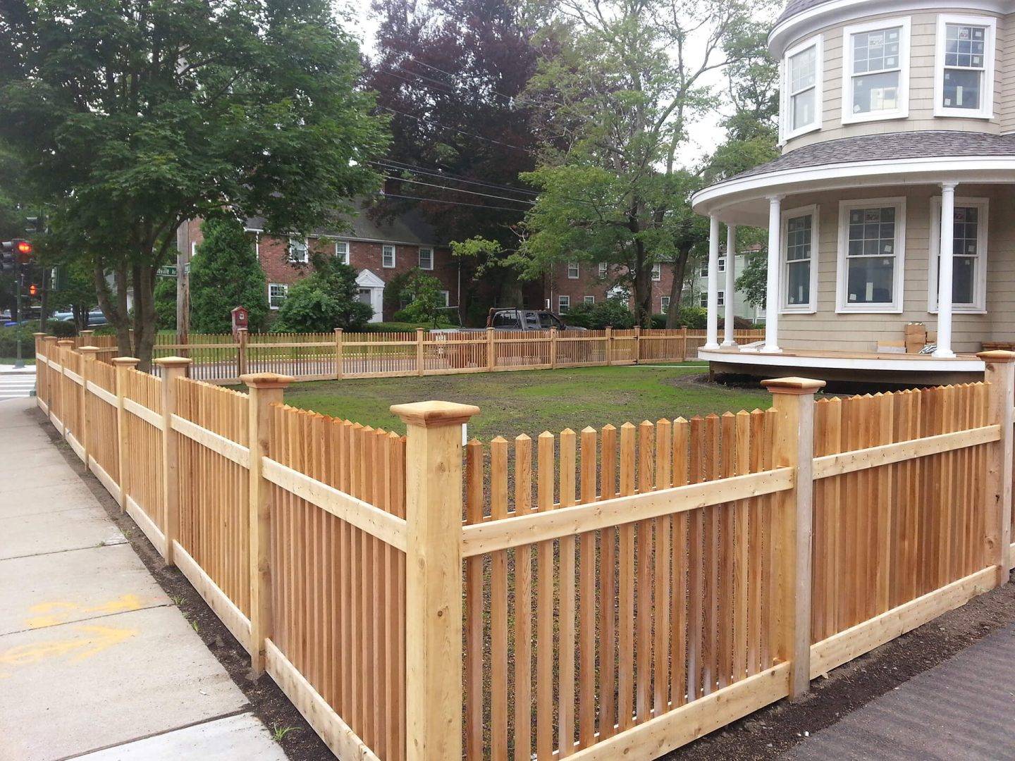 A newly constructed wooden fence in front of a house Corner section of a light colored wooden fence with grassy area