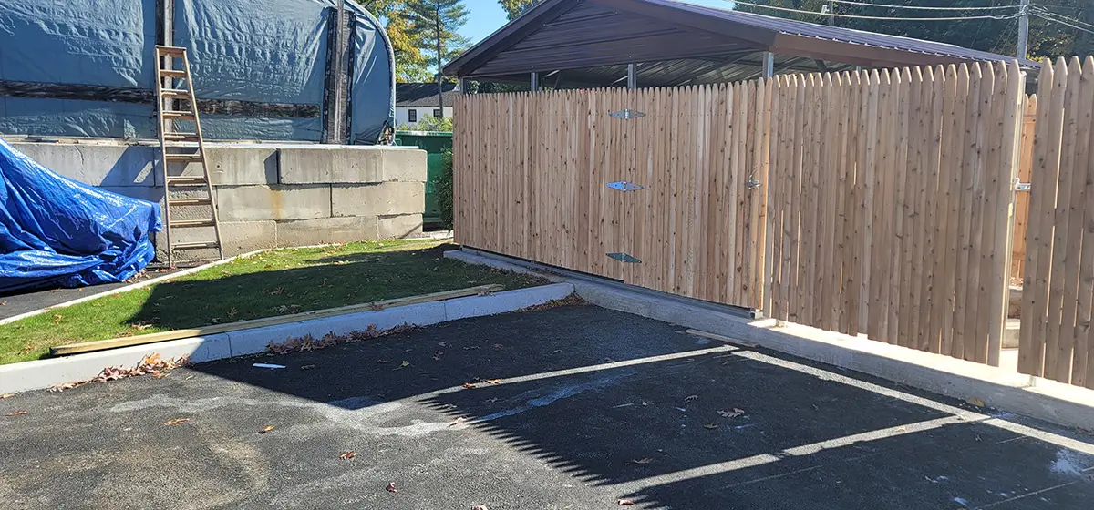 A wooden fence is being installed in a backyard, with tools and materials visible around the area.