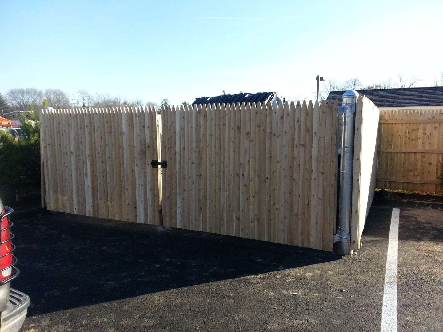 A wooden fence with a gate stands in front of a parked car on a driveway.