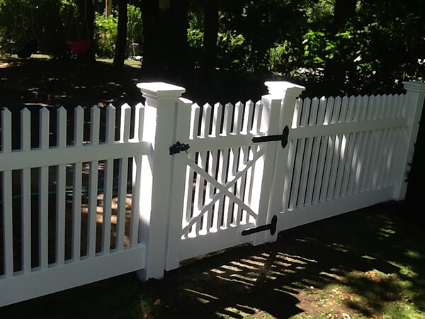 A white picket fence with a gate, surrounded by green grass and a clear blue sky.