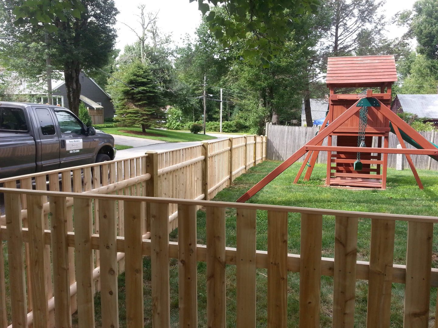 A wooden fence surrounds a backyard featuring a colorful playhouse for children.