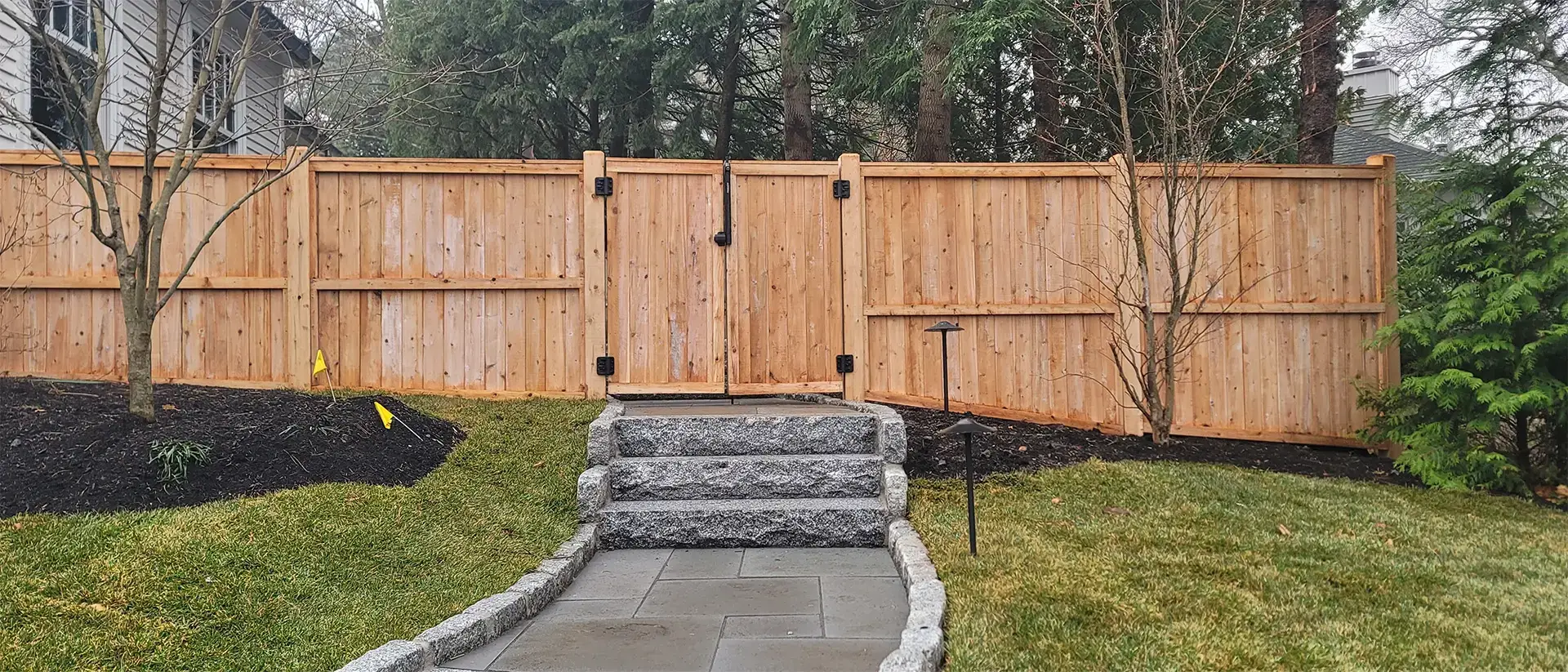 A wooden gate set within a wooden fence with stone pathway leading to up to it